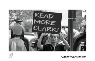 Protester holding a sign saying 'READ MORE CLARK!' during a public demonstration.