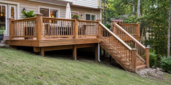 Wooden deck with stairs attached to a house, surrounded by greenery.