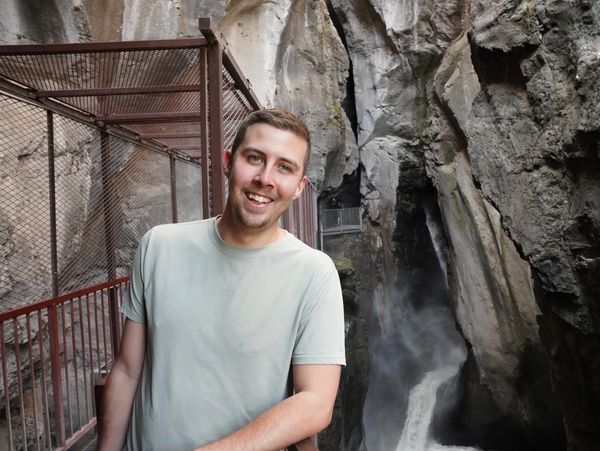 A man smiling on a metal walkway near a waterfall in a rocky canyon.