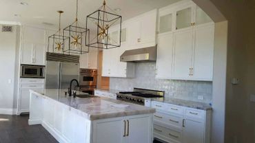 White kitchen, upper & lower white cabinets, three large pendant lights, & stainless steel appliances