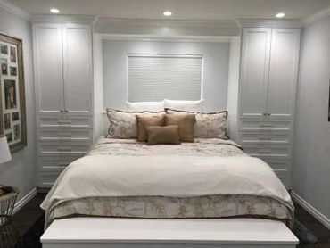 Custom white cabinets with doors & drawers and king bed in the middle with a window above the bed