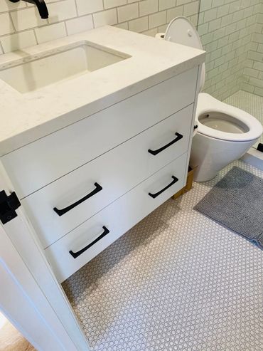 Small white bathroom cabinet with a white quartz countertop and sink with black faucets and hardware