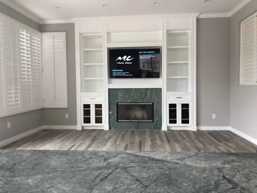White custom cabinets with a TV above a stone fireplace