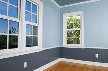 Corner of a room with two tone blue walls, white trim and moldings, and a window on each wall 