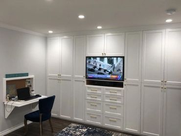 Custom wall to wall white cabinets with doors and drawers and a TV in the center