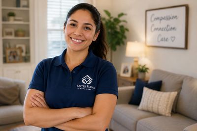 Smiling woman in a Mater Plena home care shirt stands confidently in a cozy living room.