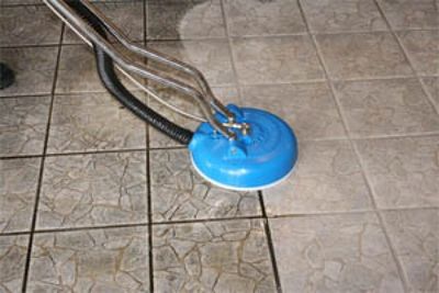 A tile floor being cleaned with a blue rotary cleaning machine.