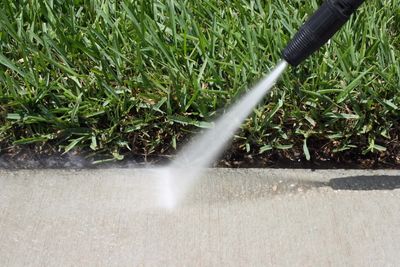Pressure washer cleaning dirt off a concrete sidewalk near grass.