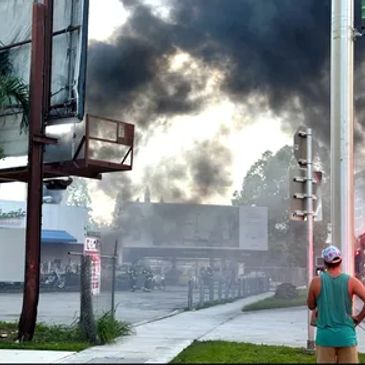 Thick black smoke billows from a building fire while a man watches.