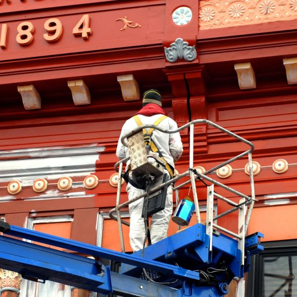 A worker painting a red building while elevated.