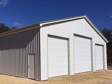 Enclosed Pole Barn with three large garage doors and one, man door and white panels.