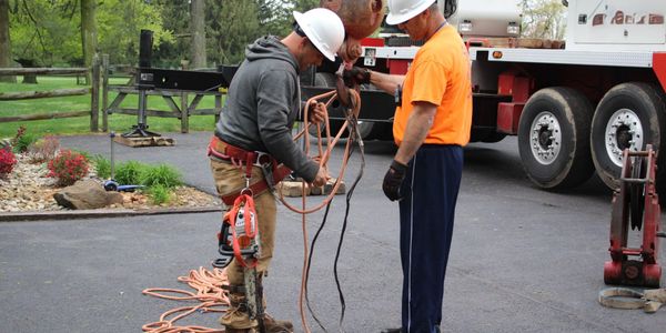 Two construction workers in safety helmets handling cables near a truck.