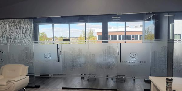 Modern office with glass walls featuring cityscape designs and cozy seating.