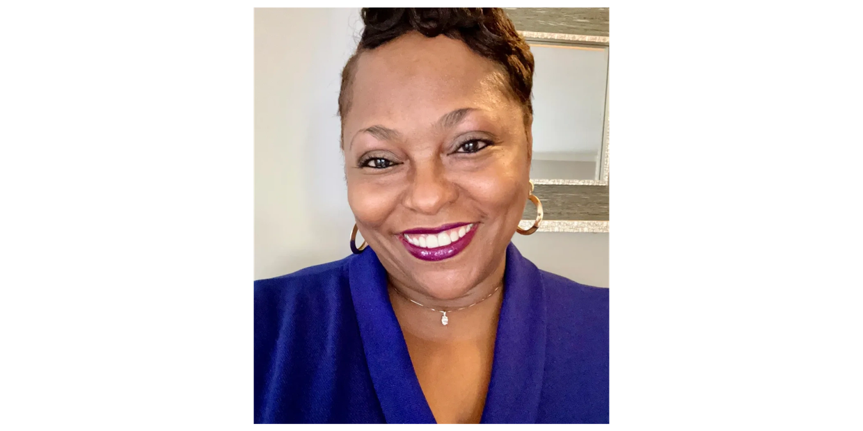 Smiling woman in blue top with gold hoop earrings.