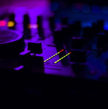 Close-up of a DJ mixer with colorful lights in a dark setting.