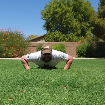 Man doing push-ups on green grass outdoors on a sunny day.