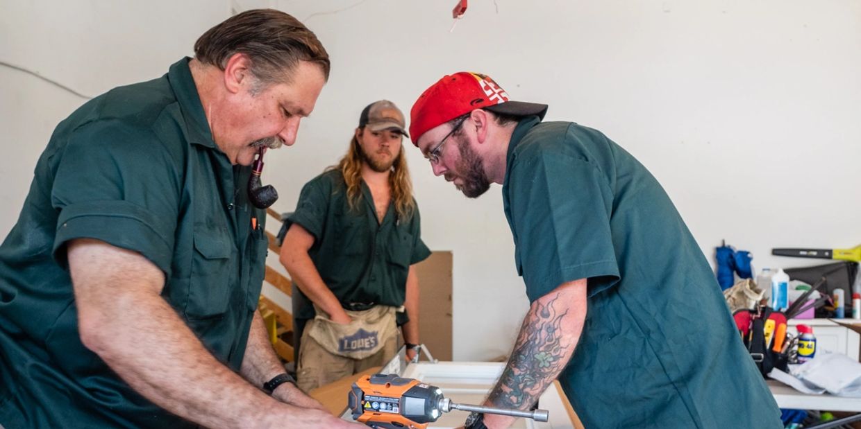 Three people working on a table wearing green shirts.