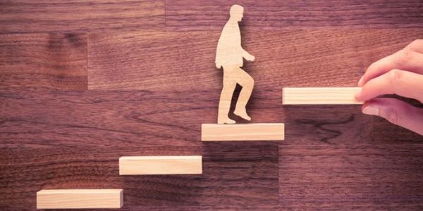 Wooden figure climbing stairs with hand placing next step.