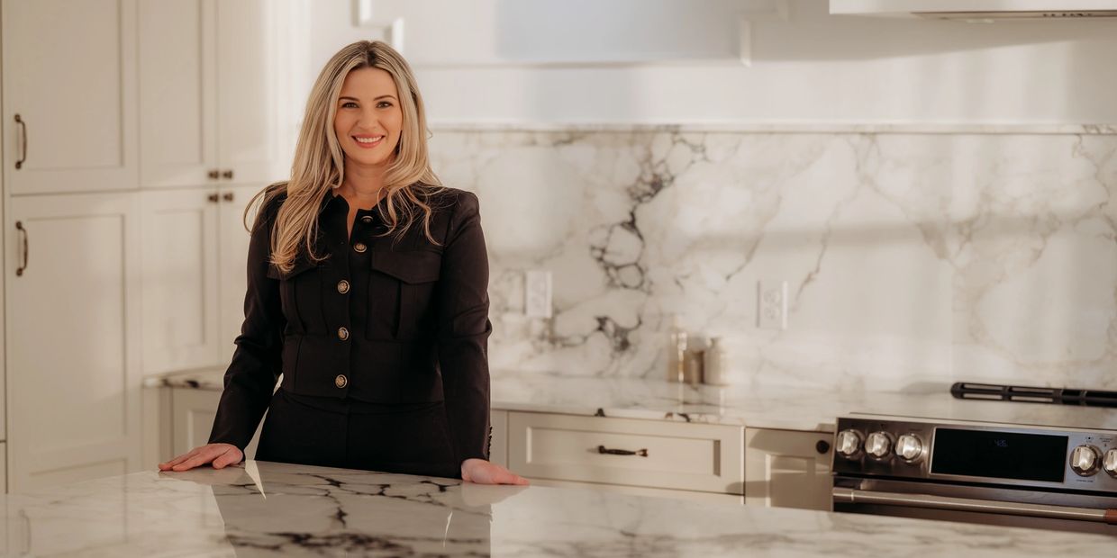 Smiling woman in black outfit standing in a modern marble kitchen.