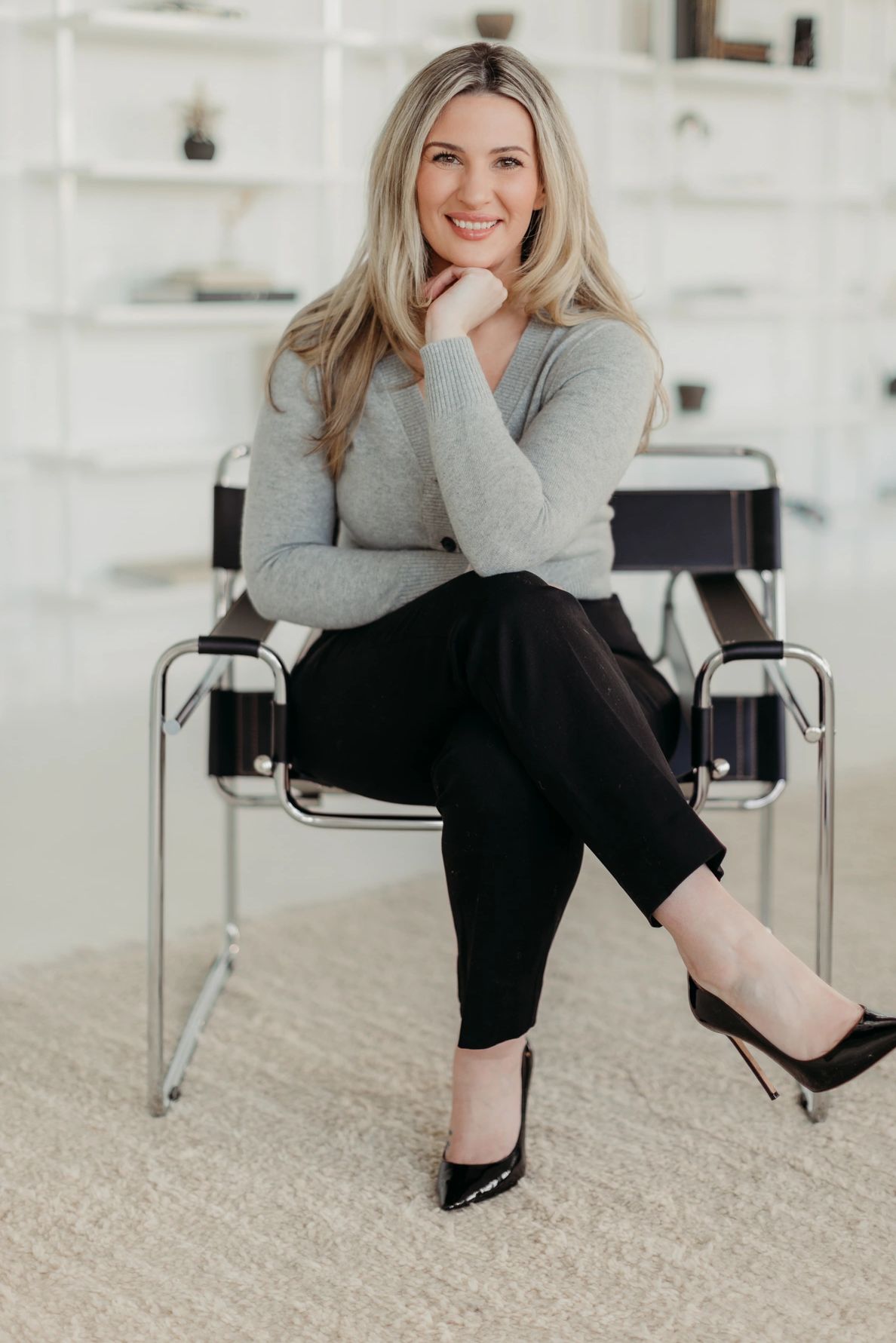 blonde professional woman sitting in a chair smiling with her hand on her chin. 