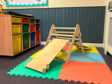 Wooden slide on colorful foam play mats in a kids' room.