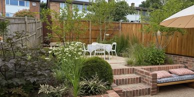 Cozy garden patio with white table and chairs surrounded by lush greenery.