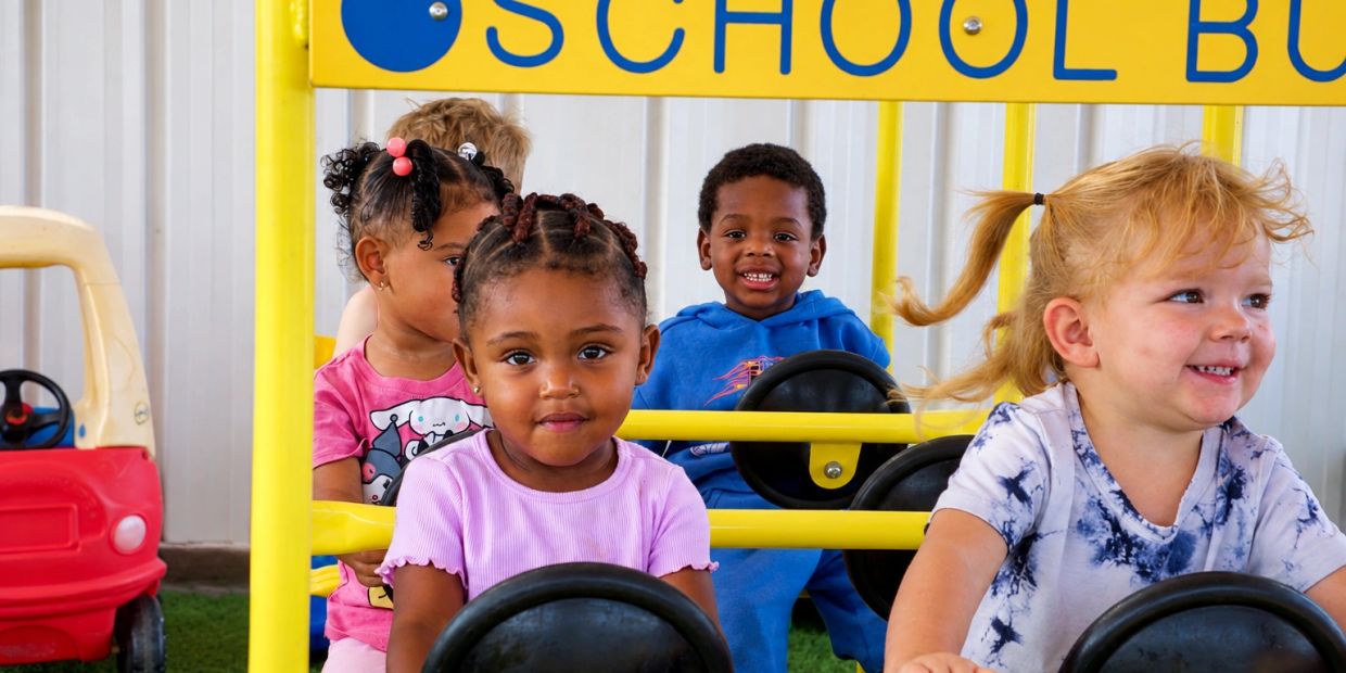 Four children playing on a yellow toy school bus indoors.