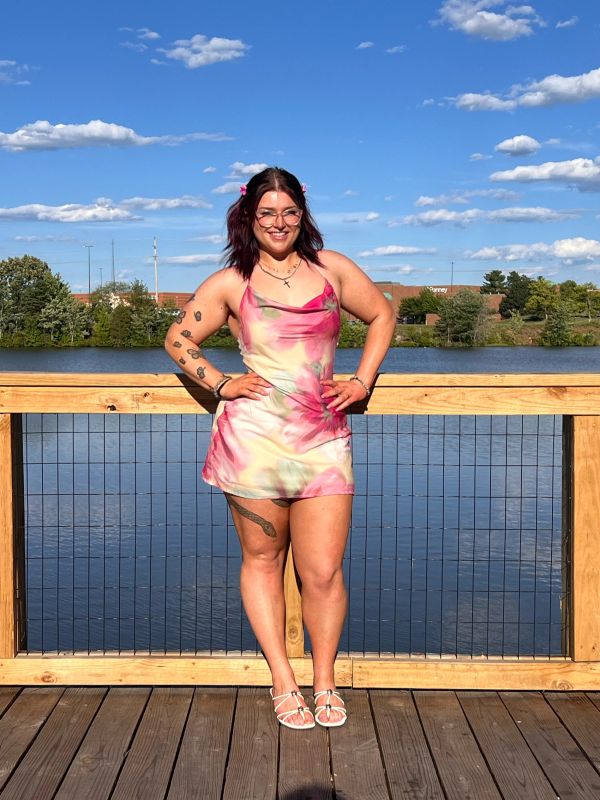 Young woman in floral dress posing on a wooden deck by the water.