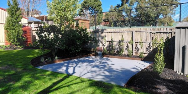 A sunny backyard with green grass, trees, and a concrete slab.