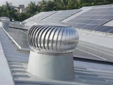 Metal roof vents and solar panels installed on a rooftop amid greenery.