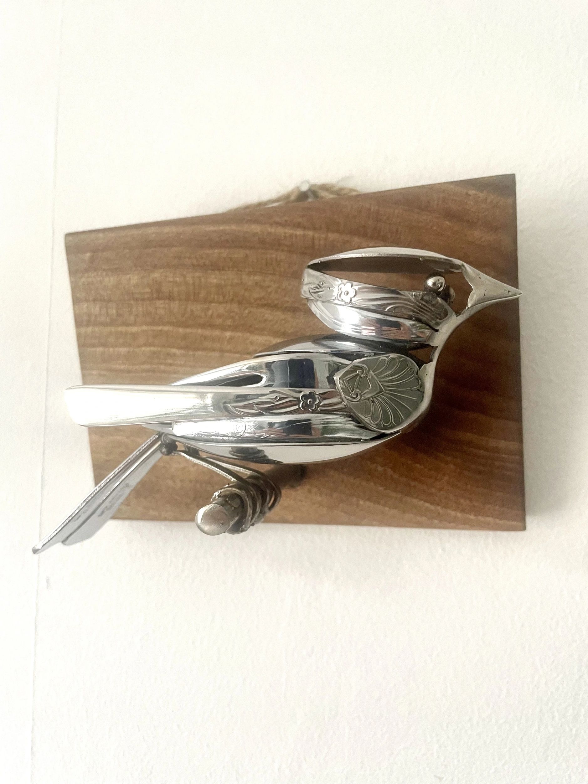Silver bird sculpture made from spoons mounted on wood.
