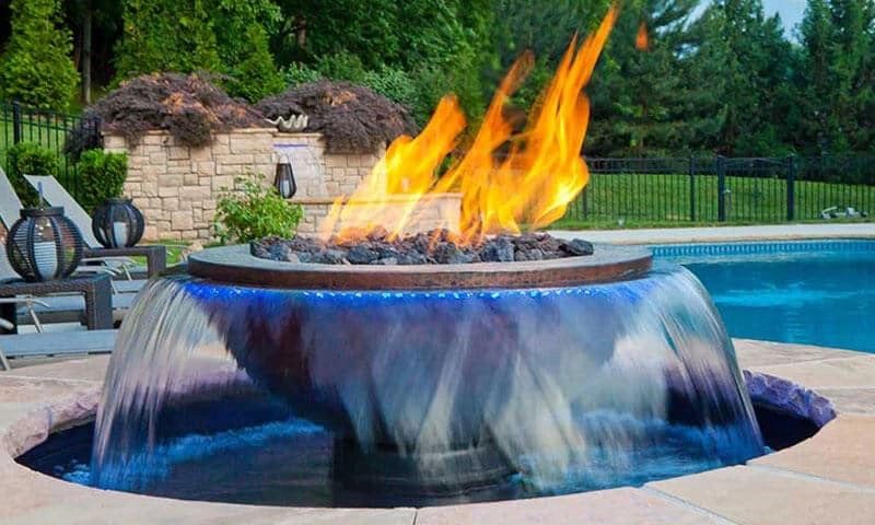 Outdoor fire pit with cascading water next to a swimming pool.