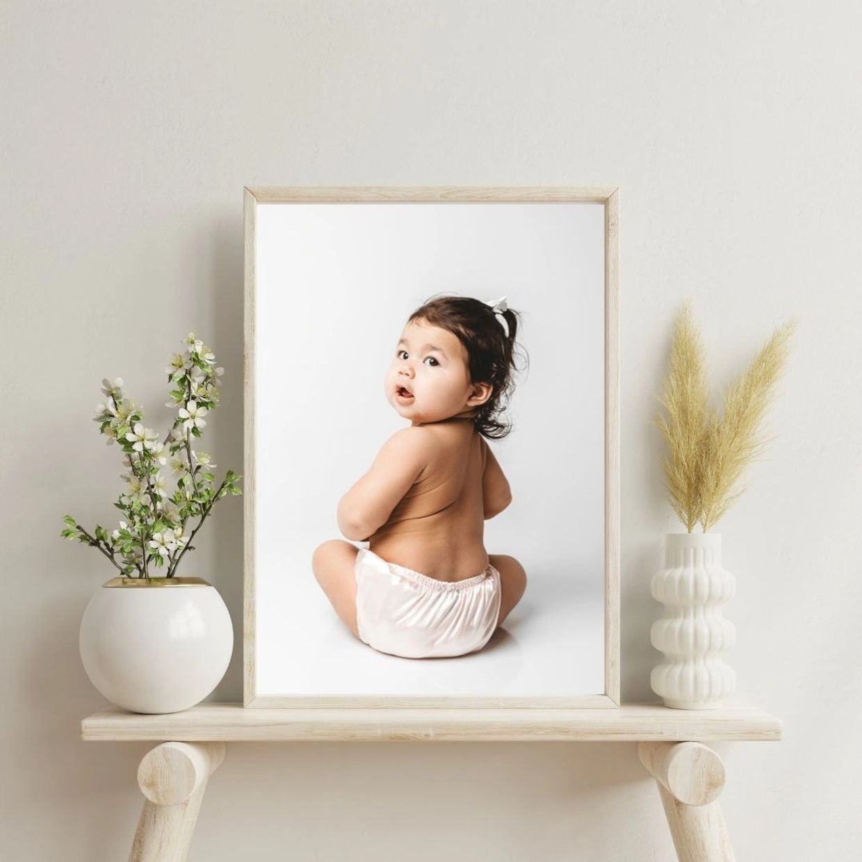 Framed photo of a baby sitting and looking back, placed between two vases with plants.