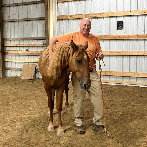 Man happily posing with a chestnut horse indoors.