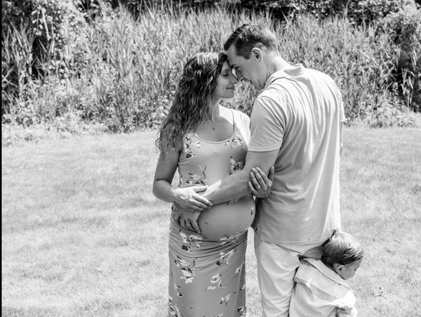 A tender moment between a pregnant woman and her partner with a child hugging him.