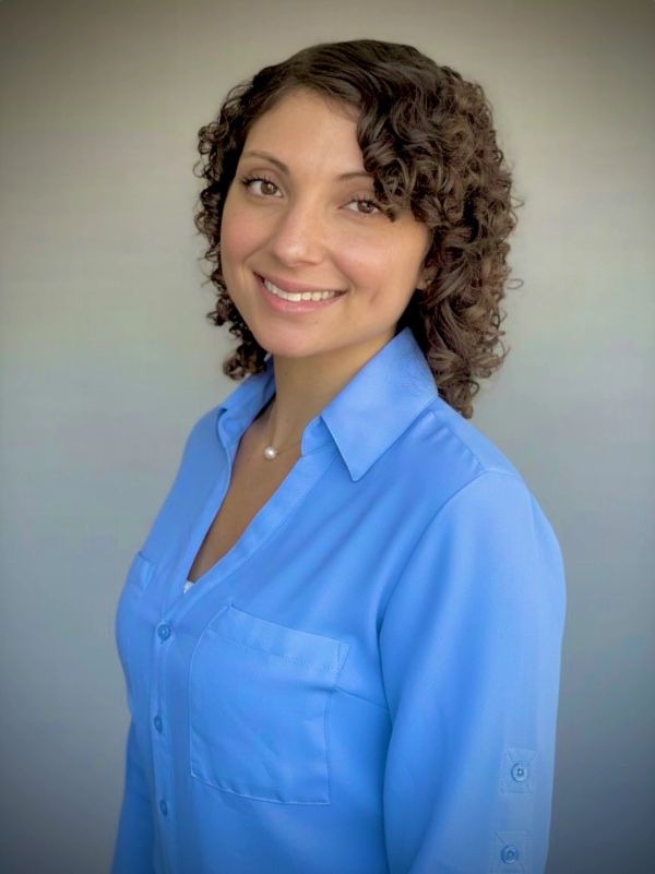 Smiling woman with curly hair wearing a blue blouse against a plain background.