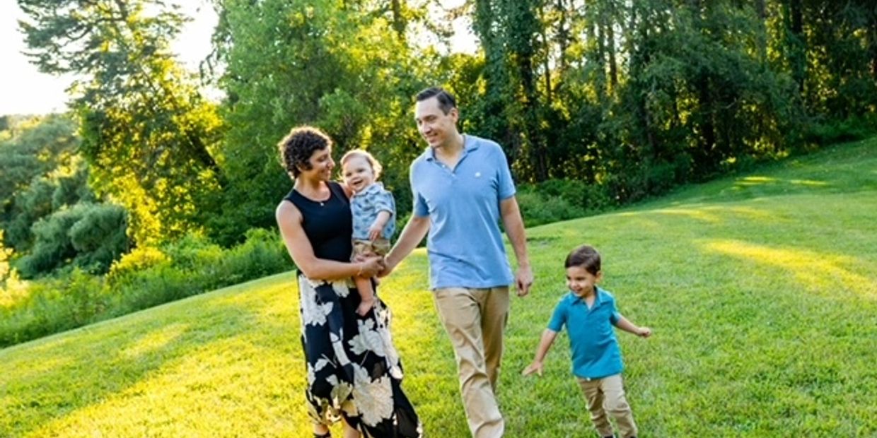 A family of four walking happily in a sunlit green park.