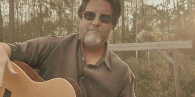Man with sunglasses playing acoustic guitar outdoors.