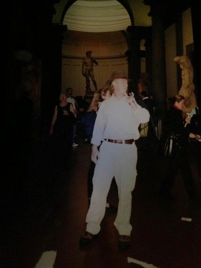 Man posing inside a dimly lit museum with statues in the background.