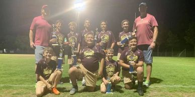 Youth baseball team posing with trophies on a field at night.