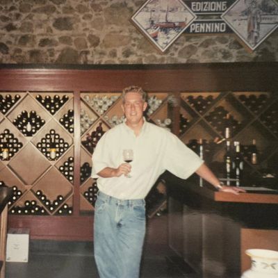 Man in casual attire holding wine glass in a wine cellar.