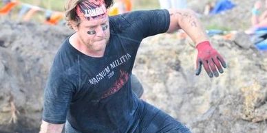 Man in athletic gear navigating a muddy obstacle course.