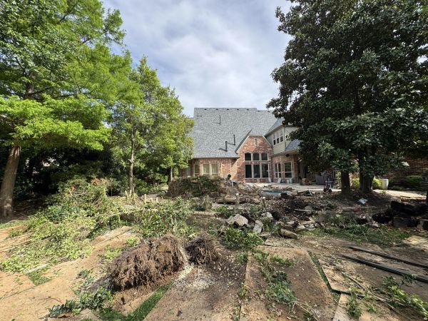 Backyard landscaping with uprooted trees and debris near a large house.