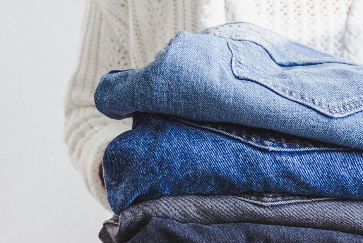 Person holding a stack of folded denim jeans in varying shades of blue.