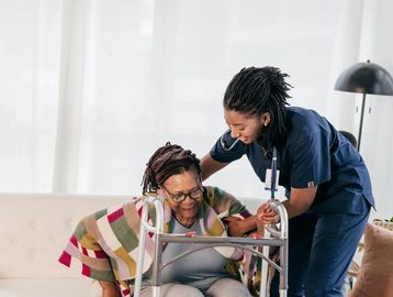 Nurse assisting elderly woman with walker in a cozy living room.
