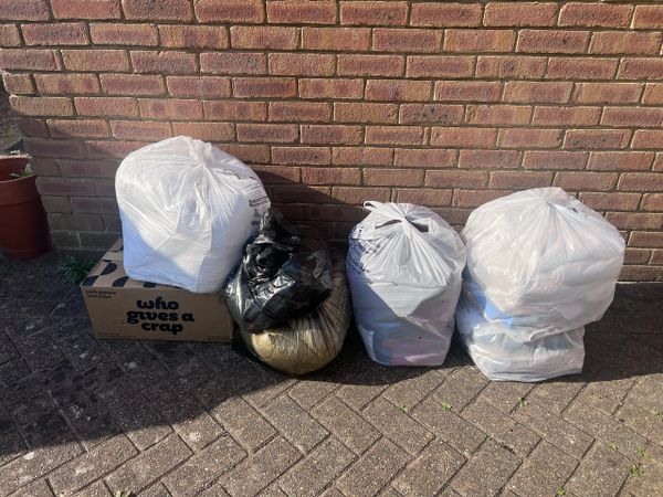 Four large garbage bags and a cardboard box are placed against a brick wall outdoors.