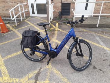 Blue Trek electric bike with saddlebag parked in a marked area outside a building.