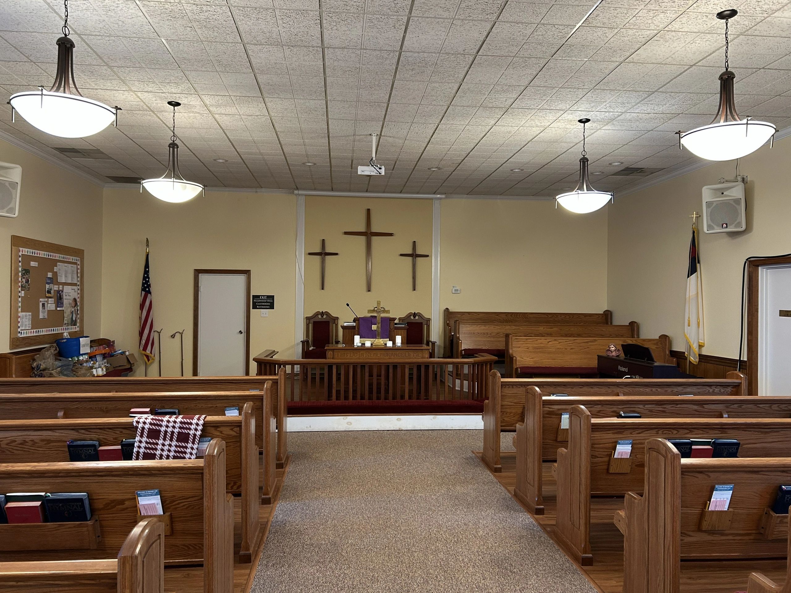 Interior of a small church with wooden pews and crosses on the wall.