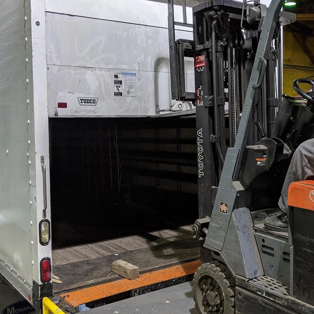 Forklift unloading wood block into an empty truck.