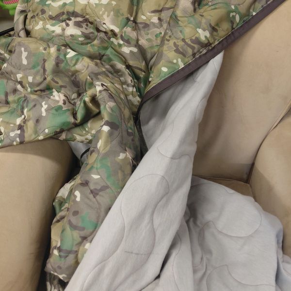A camouflage blanket draped over a beige armchair with a grey inner lining.